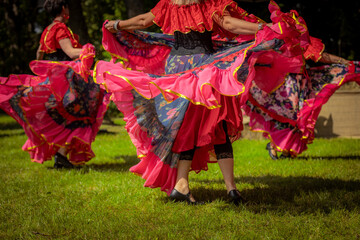 Fototapeta premium Women in colorful, ruffled dresses perform a lively traditional dance outdoors at a cultural festival, surrounded by onlookers and tents. 08.09. 2025, Jaunpiebalga, Latvia