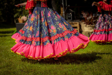 Obraz premium Women in colorful, ruffled dresses perform a lively traditional dance outdoors at a cultural festival, surrounded by onlookers and tents. 08.09. 2025, Jaunpiebalga, Latvia
