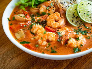 Tom Yum soup - Thai soup with shrimps, chicken and rice noodles on wooden table	