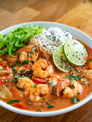Tom Yum soup - Thai soup with shrimps, chicken and rice noodles on wooden table	