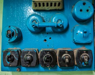 Close-up view of an vintage and old painted blue electrical switchboard with rotary switches, fuse holders, and plug sockets showing signs of age and wear.