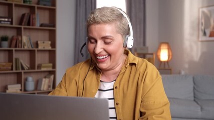 Smiling woman with headset using laptop, talking, working customer support service operator at home, in headphones with microphone. Freelance online work. Internet and technologies.
