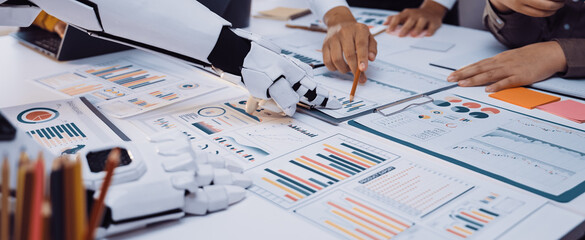 A robotic hand assists human team members in a modern office setting, collaborating on business...