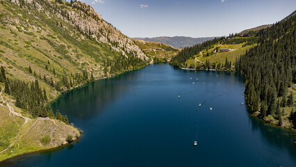 Fototapeta premium Aerial view of the stunning turquoise waters of Lower Kolsay Lake surrounded by lush pine forests and rugged mountains in Kazakhstan's Tien Shan range