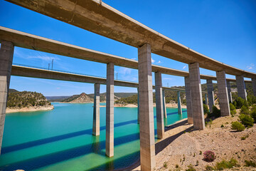 Tranquil scenery under a bridge over a reservoir with crystal clear turquoise water.
