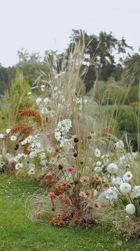 Vertical video. Flower arrangement, floral decor, flowers on the grass. Boho style wedding arch with a composition of dried flowers and pastel flowers on a green lawn, wedding ceremony in the park.