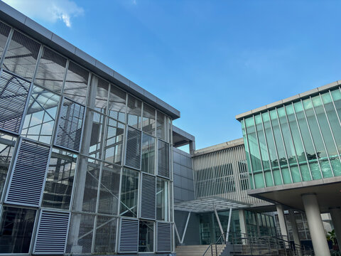 modern architectural shot of a contemporary building with large glass windows and metal louvers against a blue sky, showcasing a clean, institutional design.