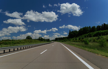Fototapeta premium Road view on a summer day. Highways and cars, roadside and white road line markings.
