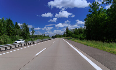 Fototapeta premium Road view on a summer day. Highways and cars, roadside and white road line markings.
