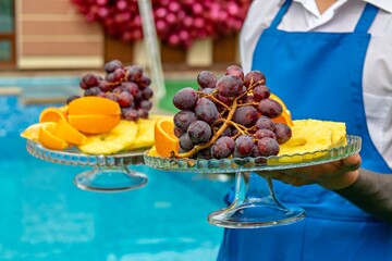 In the image there is a person holding two glass plates with a variety of fruits