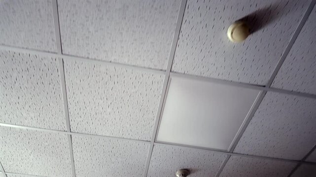 White acoustic drop ceiling with square perforated tiles in grid layout, viewed from below at diagonal angle inside commercial or institutional indoor setting