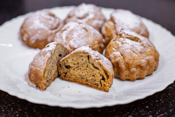 Freshly baked muffins are laid out on a white plate, revealing the inside of one muffin after being sliced and dusted with powdered sugar.