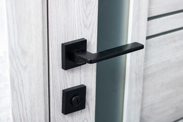 A detailed close up of a sleek black door handle on a white door