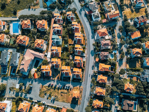 Drone capturing an aerial view of a residential neighborhood, showcasing houses with orange tiled roofs, swimming pools, and tree lined streets - Powered by Adobe