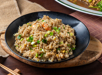 Delicious Asian Mixed Fried Rice with Shrimp, Egg, and Green Onions Served in a Black Bowl on Wooden Board Side View