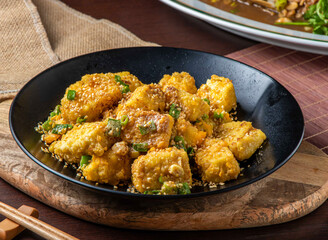 Golden Fried Jinsha Tofu with Sesame Seeds and Scallions in Black Bowl, Crispy Chinese Cuisine Closeup side view
