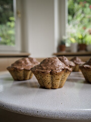 Close-up of hazelnut muffins with chocolate topping on a white plate, homemade sweet treats in natural light kitchen setting.