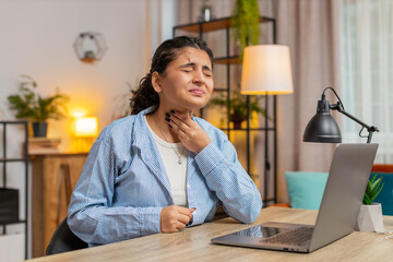 Indian woman freelancer feeling unwell sick ill suffering from sore throat hurt swallowing pain touches neck coughing working at home office workplace. Female girl has a cold, flu, virus. Lifestyle.