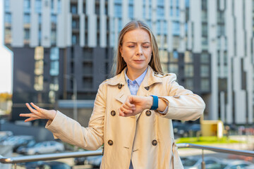 Upset mature woman standing outside office looking around waiting for business meeting impatient girl dissatisfied looks at the wristwatch, checks time on watch annoyed by being late lateness concept.