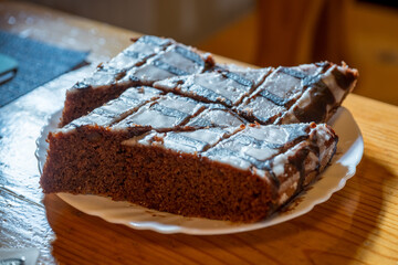 A brown chocolate cake with icing on a white plate.
