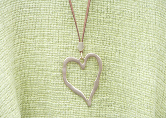 Elegant gold heart necklace on a leather strap laying on green woven fabric