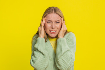 Displeased exhausted Caucasian middle-aged woman rubbing temples to cure headache problem suffering from tension migraine stress. Adult girl grimacing in pain, high blood pressure on yellow background