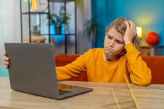 Caucasian teenager boy receiving bad news on laptop at home. Seeing poor education exam results negative grades at school, sitting gloomily on couch by table, looking at screen with sad expression
