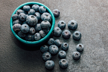 Fresh blueberries in a turquoise bowl on a textured surface