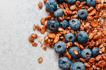 Fresh blueberries mixed with crunchy granola on a light gray surface during morning hours