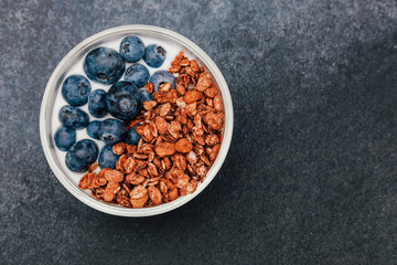 Healthy breakfast bowl with yogurt granola and blueberries on dark background