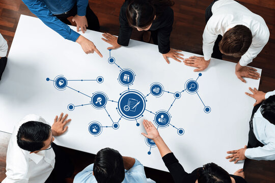 A diverse team gathered around a table, examining various icons and data points, showcasing collaborative efforts in strategic planning and decision-making processes. Amity
