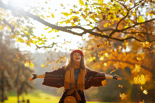 Hello autumn. smiling modern woman in red hat with scarf, gloves and bag rejoicing in the city park.