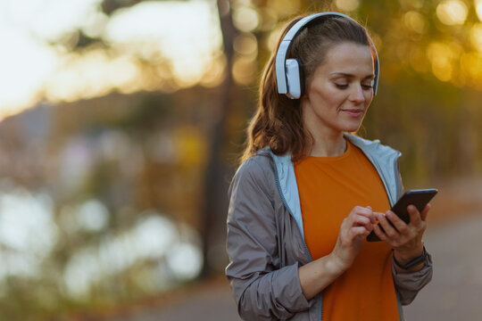 Hello autumn. trendy 40 years old woman in fitness clothes in the park with headphones.