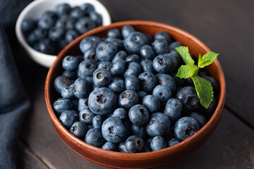 Fresh blueberries in brown ceramic bowl on wooden table background, closeup view. Summer berry harvest