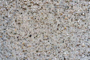 Background of rough concrete wall, where the pebbles used for the concrete mixture can be seen.