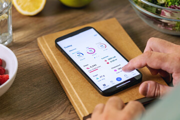 Close-up of a man's hands using a smartphone health app on a wooden table. Healthy lifestyle concept
