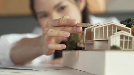 Closeup of young beautiful architect engineer drawing blueprint while looking at architectural model to analyze house construction. Project manager point house model during taking a note. Manipulator. - Powered by Adobe