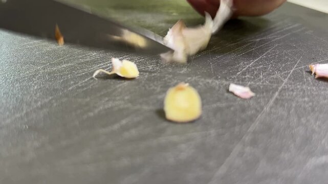 Close-up of hands chopping fresh garlic cloves on a cutting board for cooking preparation