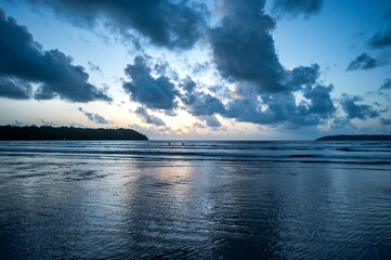 View of the Arabian Sea from Miramar Beach, Goa, at dusk after sunset, with grey clouds, orange glow in the sky, low waves, and backlit cliffs creating a serene monsoon coastal scene.