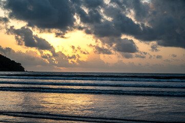 Sunset view of Vagator Beach Goa with Arabian Sea, golden yellow sky, dramatic grey monsoon clouds, and shimmering water reflecting the sun’s warm light in the evening.