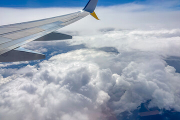 View of a white cloudscape with a wing of an airplane visible from the window concept of travel agency, aviation company, vacation planning