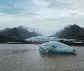 Glacier tongue slides from the Vatnajokull icecap or Vatna Glacier near subglacial Oaefajokull volcano, Iceland. Glacial lagoon with ice blocks and surrounding mountains.