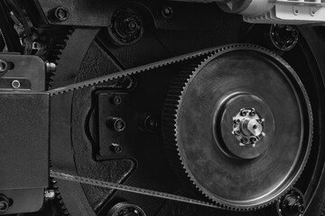 Close-up of a machine with  gear as part of large industrial mechanism, belt transmission.  gear is surrounded by other gears, and machine itself is black. Industrial concept background.