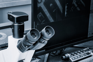 A microscope for testing the quality of products is on the table next to the computer monitor. Quality testing concept