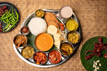 Traditional Goan fish thali featuring rice, fried fish, crab xacuti, tisryo, gulab jamun, papad, curry, and pickle, served on a plate over a wooden textured background, styled with red dried chillies