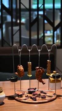Display shot of two chicken tangdi kebabs and two mutton seekh kebabs on a barbecue curve kebab stand with dips, sauces, and a wooden platter, styled for a buffet.