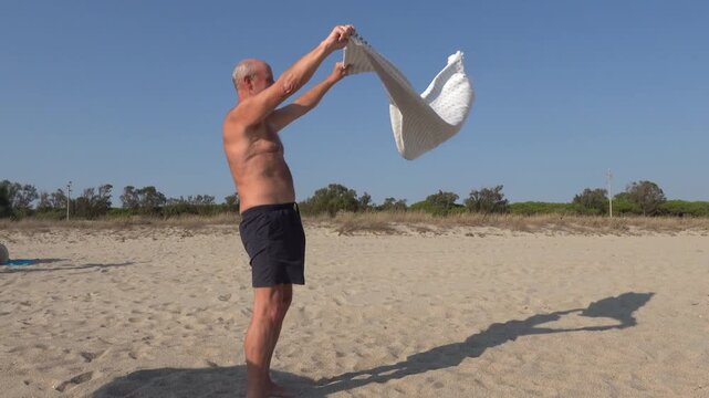 Oristano, Sardinia, Italy A man on a beach empties sand from a beach towel in strong wind. 