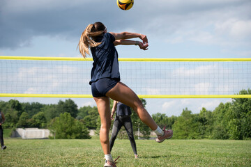 Woman jumps to pass the ball during a grass doubles volleyball game