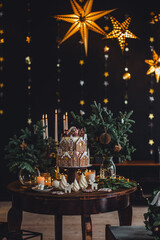 Family holiday celebration. Beautiful traditional homemade gingerbread house. Celebration of Christmas and Happy new year at home. Festive mood, cozy atmosphere, burning candles, fir tree branches