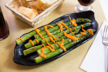 Grilled green asparagus served with romesco sauce on black plate. Catalan cuisine..